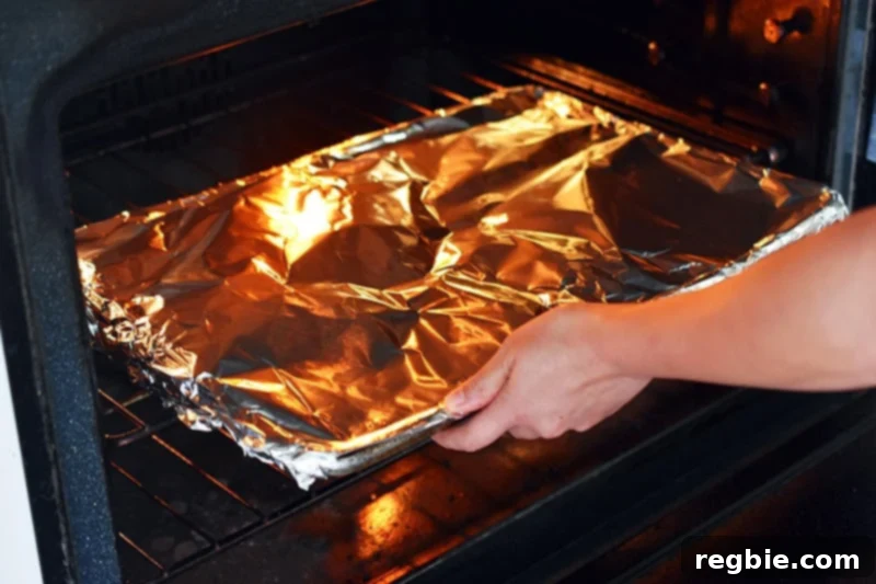 A foil-covered rimmed baking sheet, laden with seasoned cauliflower florets, is carefully placed into a hot oven.
