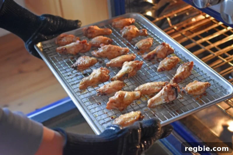 Someone taking out the tray of perfectly baked, golden-brown chicken wings from the oven, ready to serve.