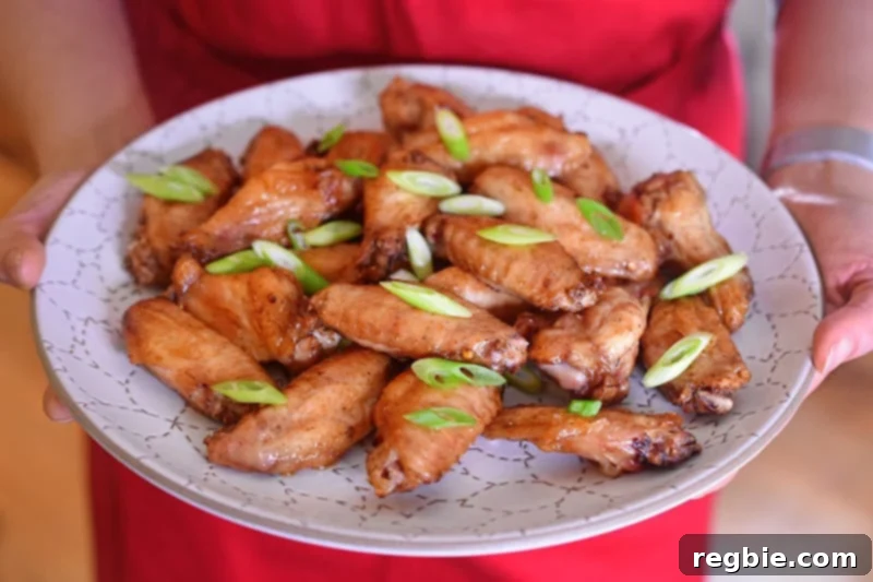 Someone holding a plate of baked chicken wings garnished with scallions and lime wedges, showcasing the delicious final product.