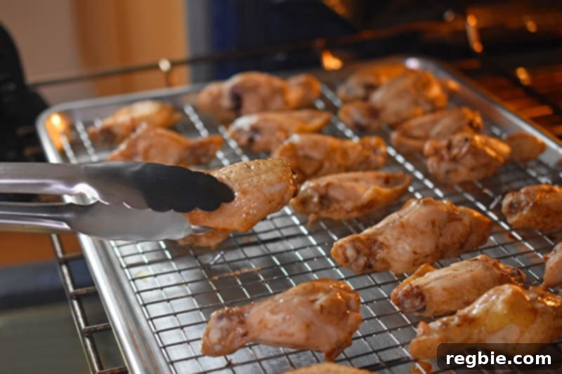 Flipping the baked chicken wings on the wire rack with tongs to ensure even crispiness and browning.