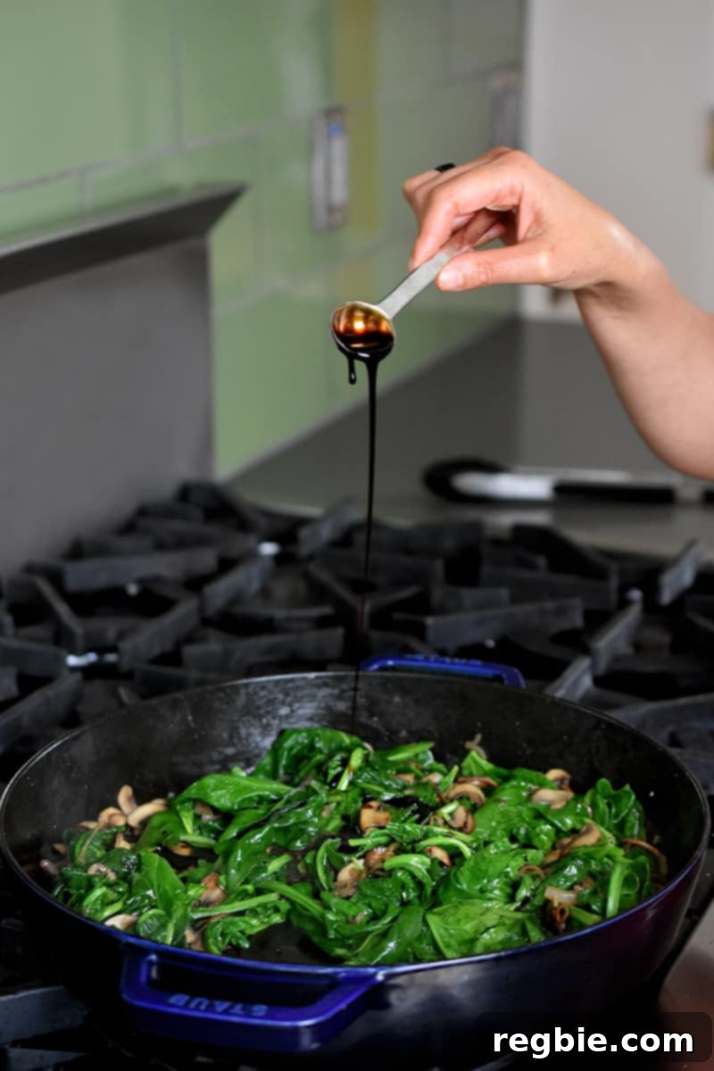 Sizzling Bacon, Mushroom, and Spinach Skillet 13 A woman in a red apron is joyfully sprinkling golden-brown crispy bacon bits generously on top of a serving bowl filled with vibrant sautéed spinach and savory mushrooms.