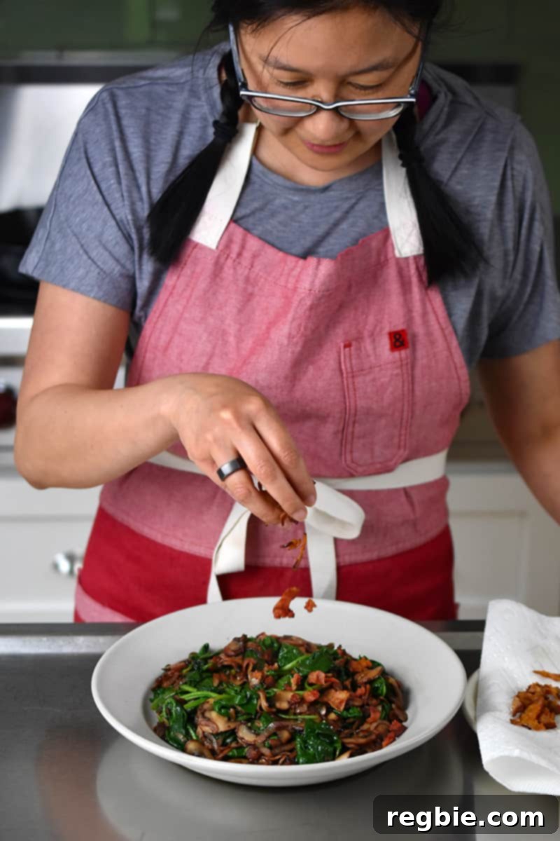 Sizzling Bacon, Mushroom, and Spinach Skillet 14 Two hands hold a cream-colored bowl filled with a delightful serving of sautéed spinach, crispy bacon, and tender mushrooms, perfectly prepared and ready to be enjoyed.