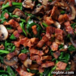 An overhead shot of a plate filled with sautéed spinach, crispy bacon bits, shallots, and mushrooms.