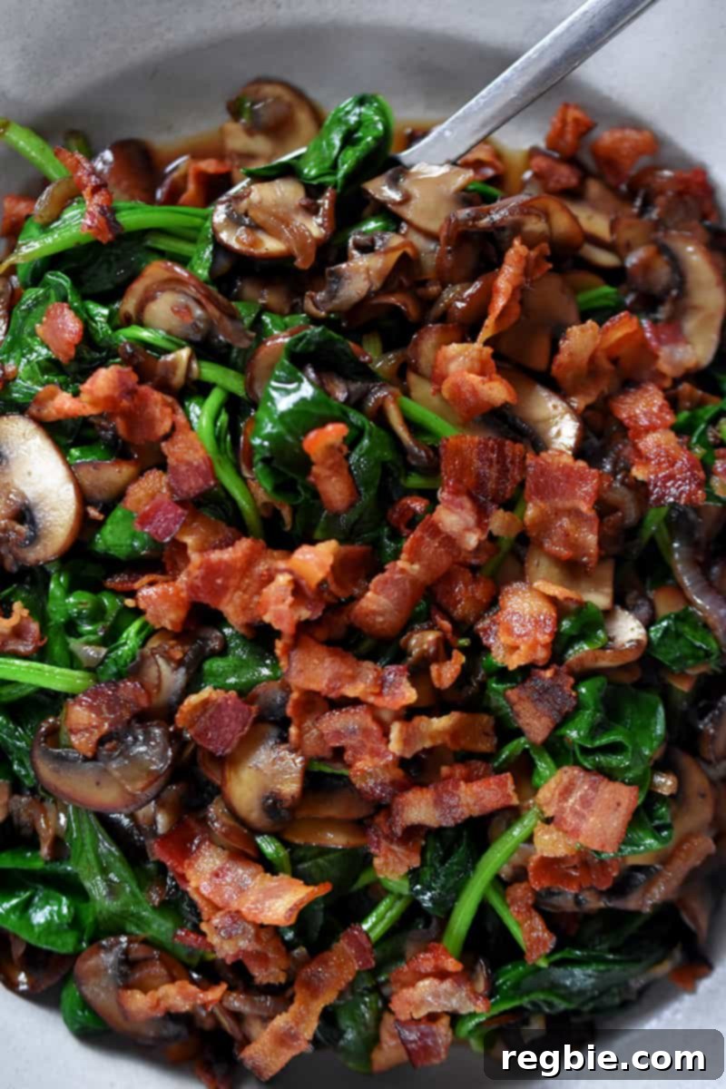 Sizzling Bacon, Mushroom, and Spinach Skillet 3 An overhead shot showcasing a rustic skillet filled with perfectly sautéed spinach, golden-brown cremini mushrooms, and scattered crispy bacon bits, ready to be served as a wholesome side dish.