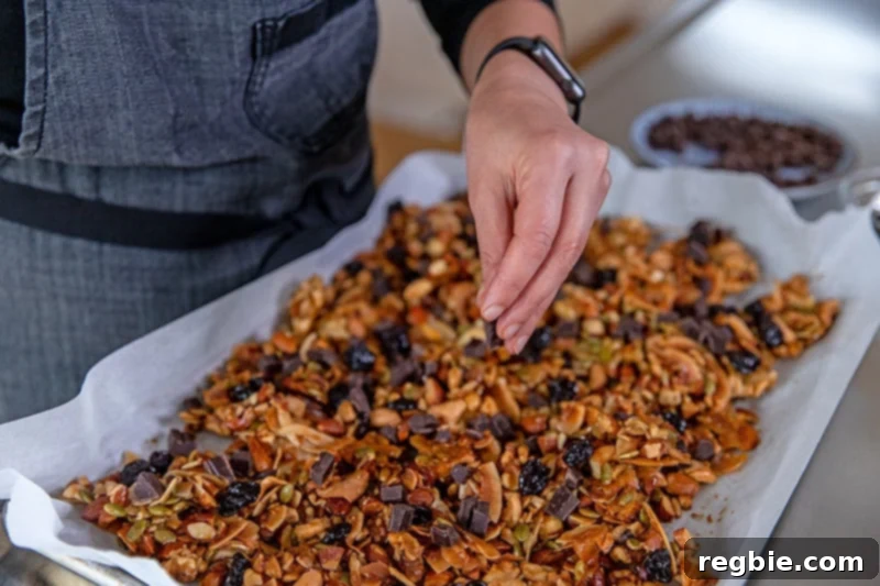 Indulgent Chocolate Cherry Granola Paleo Vegan Gluten Free 13 Someone adding dark chocolate chunks and dried cherries to cooled paleo granola on a rimmed baking sheet.
