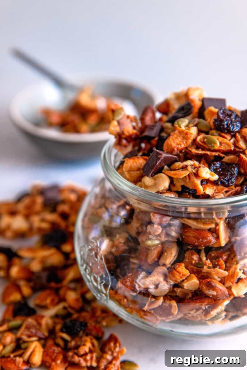 Indulgent Chocolate Cherry Granola Paleo Vegan Gluten Free 14 A closeup of a jar filled with Chocolate Cherry Paleo granola and a bowl in the background with granola on top of coconut yogurt, illustrating how to store and serve.