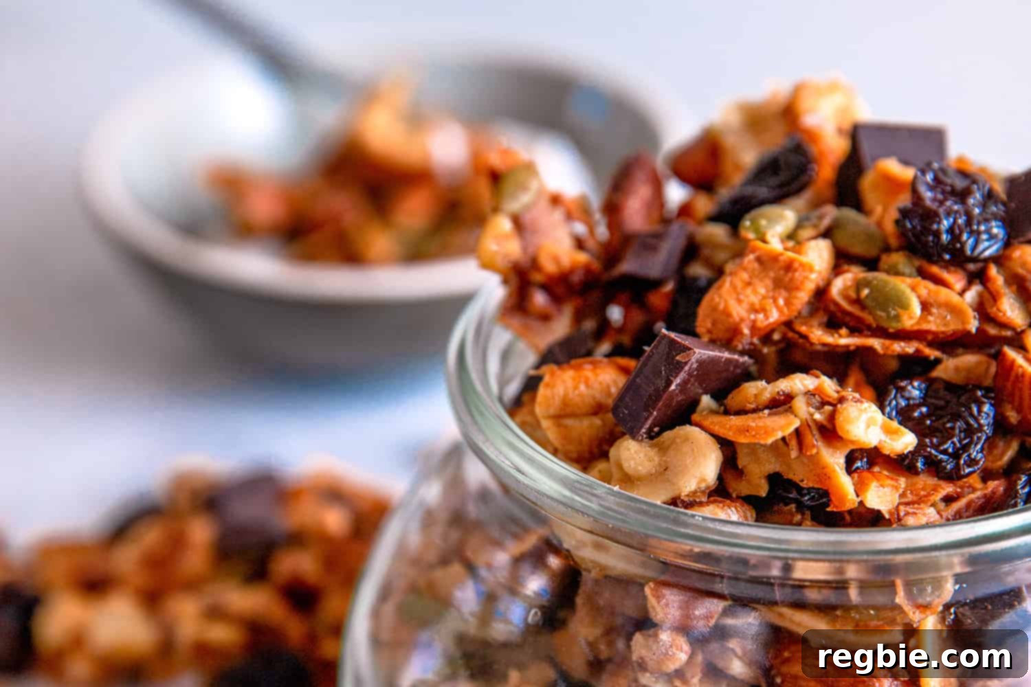 Indulgent Chocolate Cherry Granola Paleo Vegan Gluten Free 4 A close up of cherry chocolate paleo granola in a clear jar and a bowl of granola on top of coconut yogurt in the background, showcasing its delicious texture and serving suggestion.