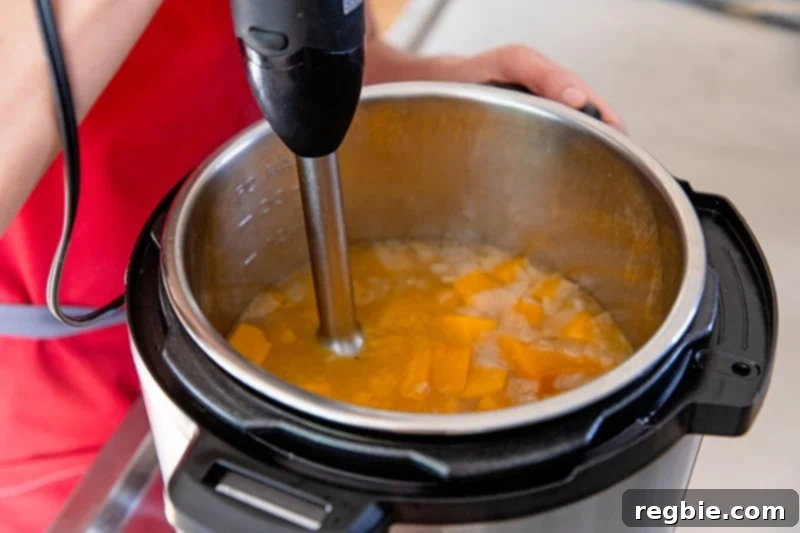 An overhead shot of an immersion blender in a pot of Instant Pot butternut squash soup.