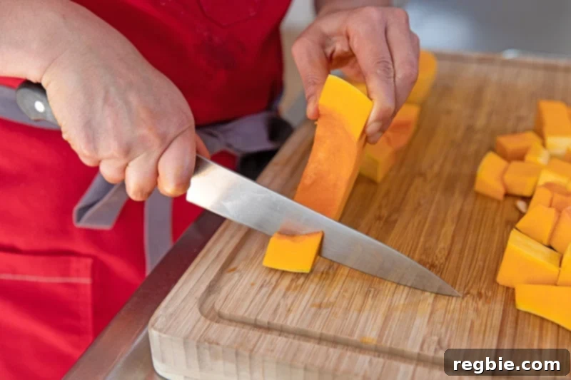 A person in a red apron is cutting a butternut squash into cubes.
