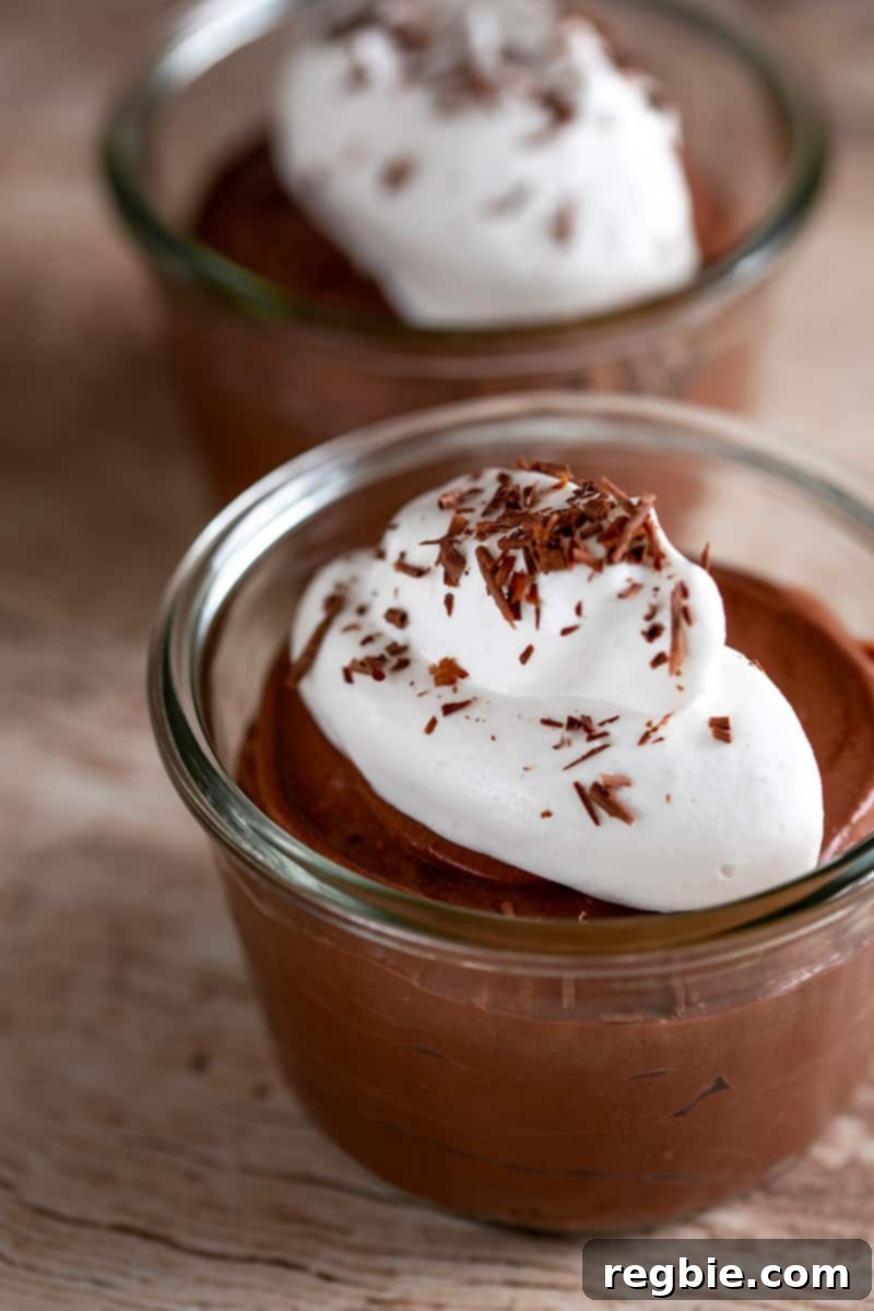 Heavenly Paleo Chocolate Pudding 2 Two clear bowls filled with paleo chocolate pudding made with coconut milk and gelatin. The dairy-free chocolate pudding is topped with a dollop of whipped coconut cream and shaved dark chocolate.