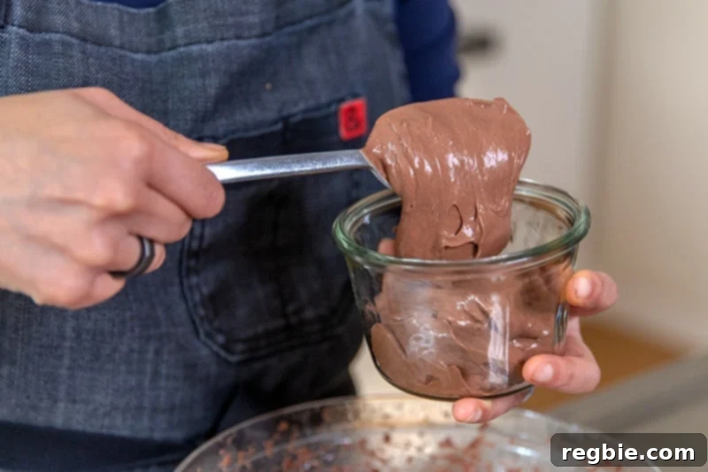 Heavenly Paleo Chocolate Pudding 10 Someone spooning dairy-free paleo chocolate pudding into a glass container.