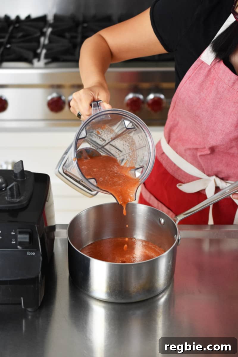 Pouring blended diced tomatoes into a saucepan as the base for the soup.