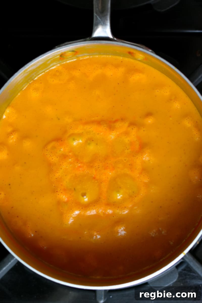 An overhead shot of the creamy dairy-free tomato soup gently simmering in a saucepan, with steam rising.