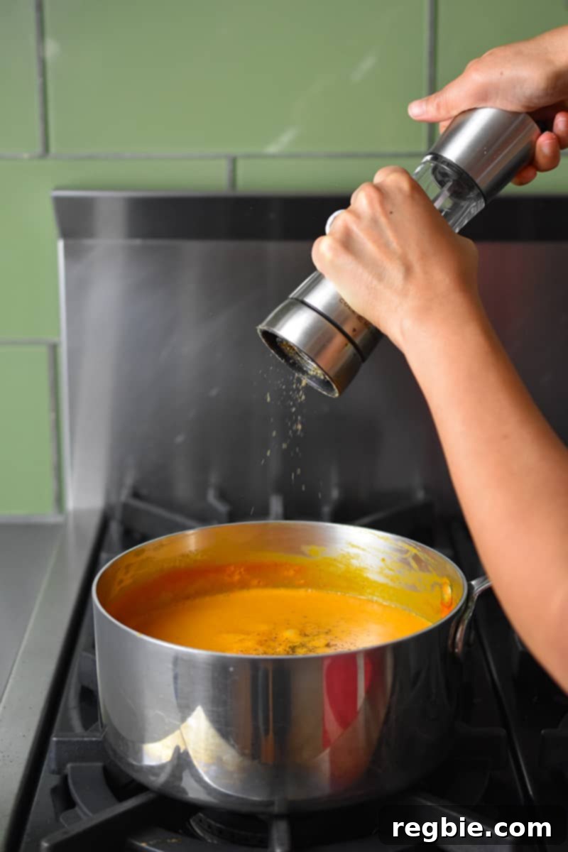 Someone cracking fresh black pepper directly into a saucepan of simmering creamy tomato soup.