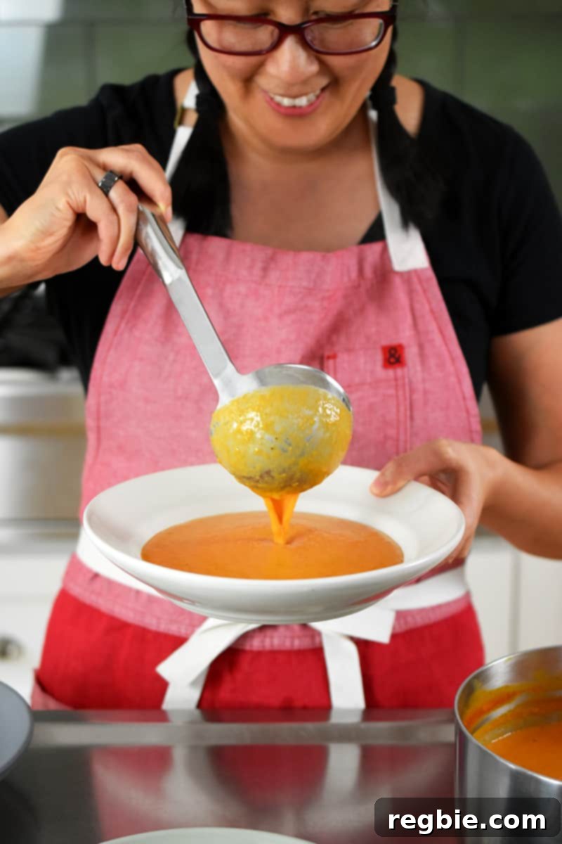 A smiling chef ladling a generous portion of creamy tomato soup into a rustic bowl.