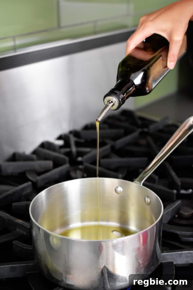 Pouring olive oil into a large saucepan for sautéing ingredients for dairy-free tomato soup.
