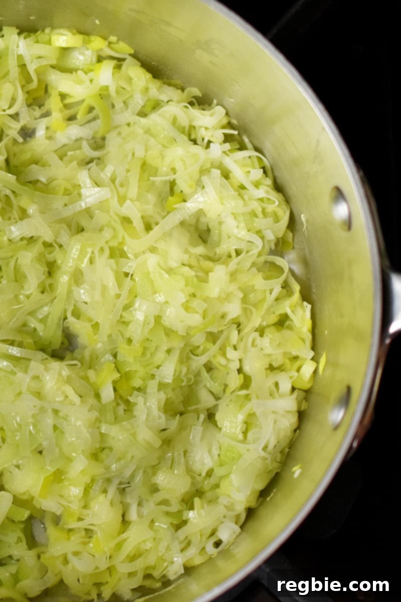 An overhead shot of softened, thinly sliced leeks gently cooking in a large saucepan.