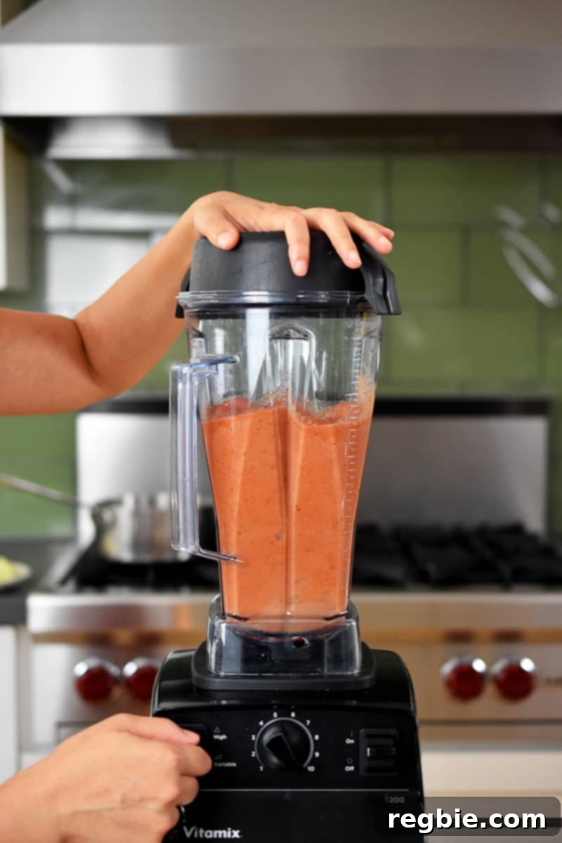 A Vitamix blender actively blending diced canned tomatoes into a smooth, vibrant purée.