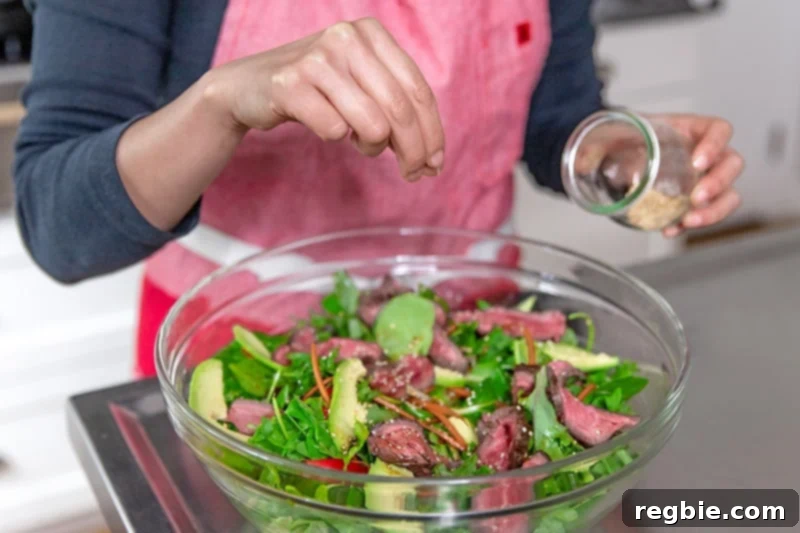 Sprinkling toasted sesame seeds on top of paleo and Whole30 Asian Steak Salad.