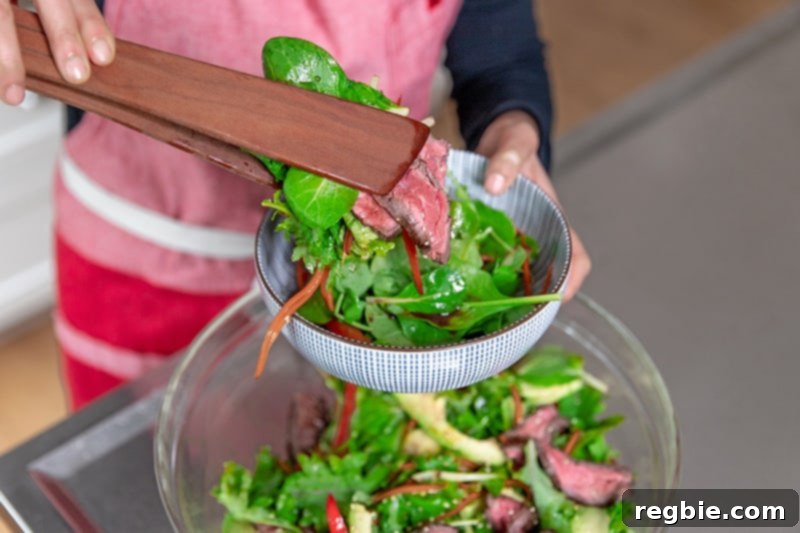 Using wooden tongs to place Asian Steak Salad into a bowl.