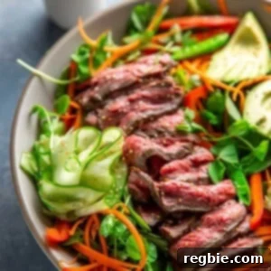 An overhead shot of Whole30 and Paleo Asian Steak Salad, a large white bowl topped with colorful vegetables and sliced seared flank steak.