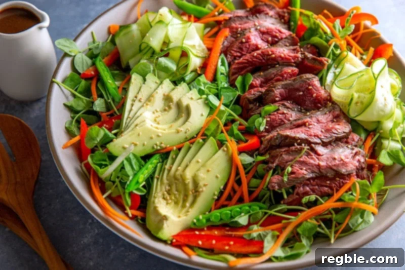 A side shot of a beautiful Whole30 Asian Steak Salad with a container of salad dressing on the side.
