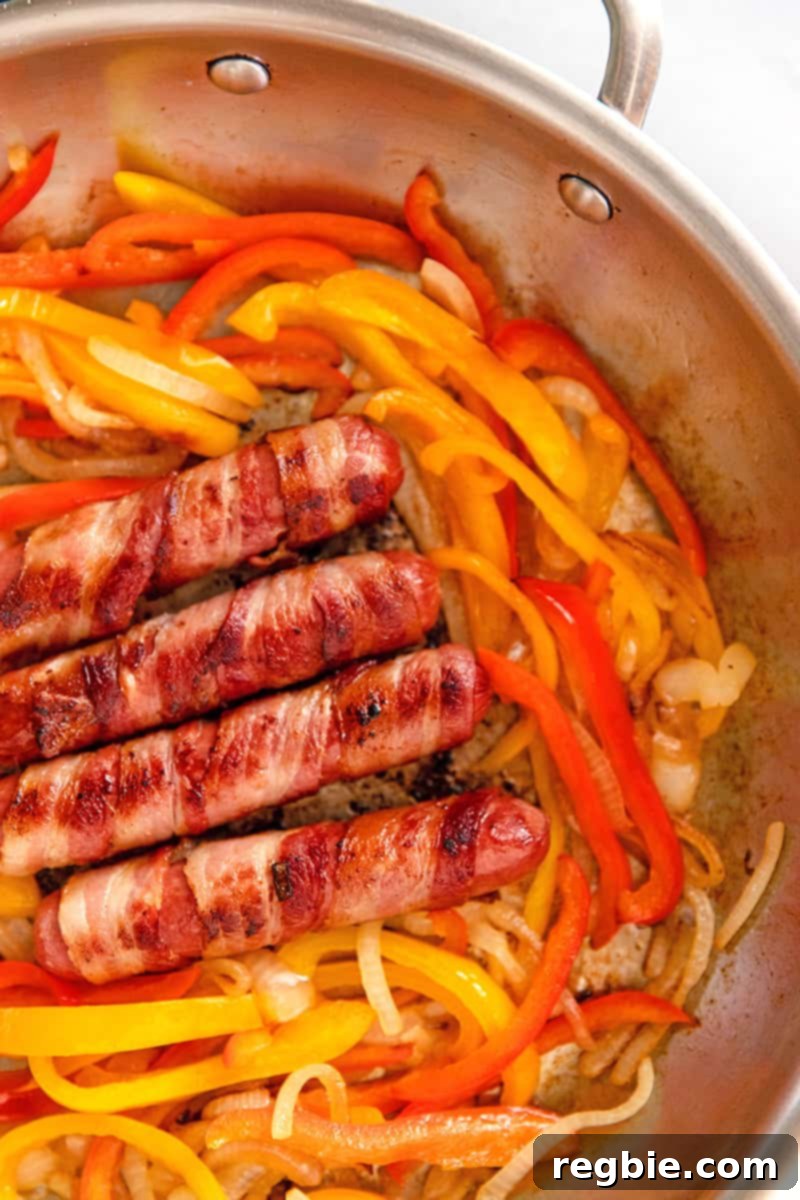 An overhead shot of paleo, keto, and Whole30 Sonoran hot dogs in a skillet with sliced onion and red and yellow bell peppers.