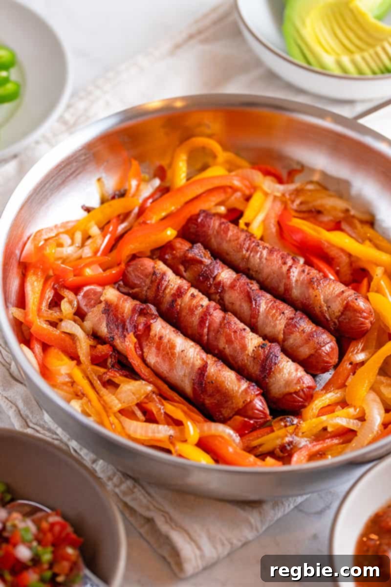 A shot of a skillet filled with Sonoran hot dogs and fried onions and peppers. Next to it are plates filled with avocado and salsa. 