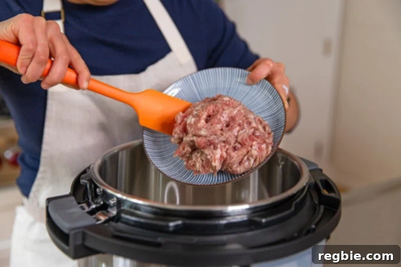 Easy Instant Pot Meat Sauce Whole30 Keto 4 A person adding bulk Italian sausage to an open Instant Pot