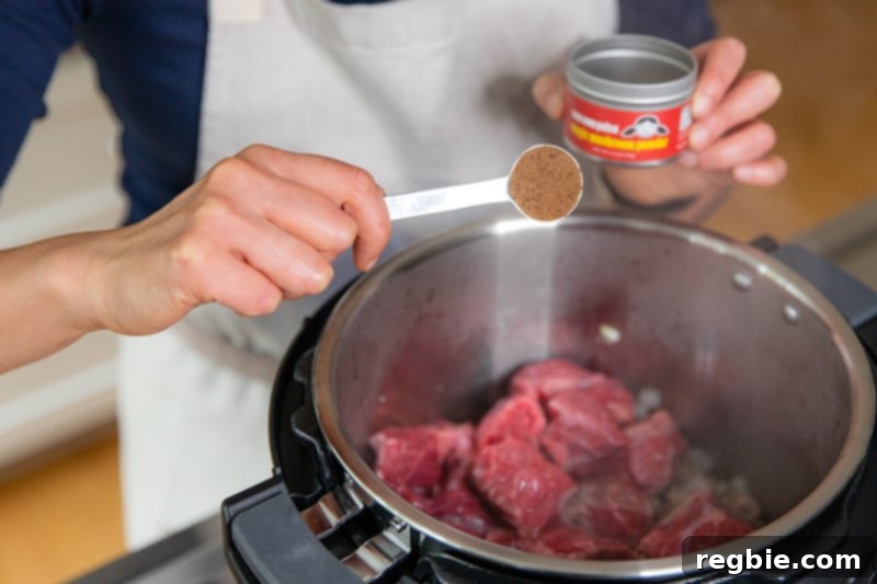 Easy Instant Pot Meat Sauce Whole30 Keto 6 Adding a teaspoon of Nom Nom Paleo Magic Mushroom Powder to the cubed chuck roast and cooked sausage and onions in an open Instant Pot.