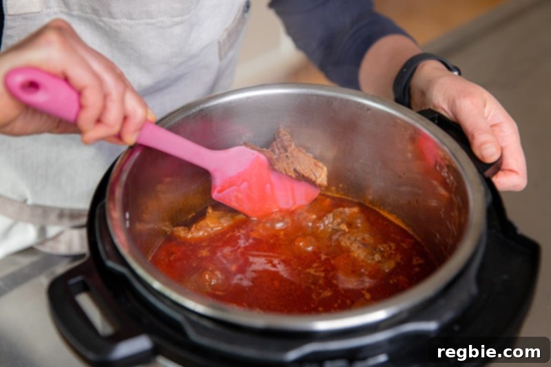 Easy Instant Pot Meat Sauce Whole30 Keto 10 An overhead shot of someone stirring a pot of Instant Pot meat sauce with a pink silicone spatula. The spatula is smushing a piece of beef agains the side of the insert to break it up.