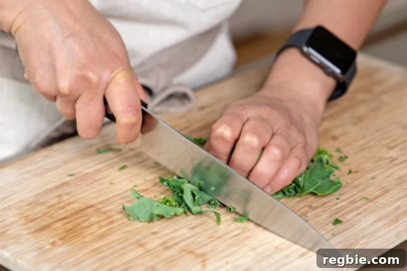 Slicing kale leaves into thin strips with a chef's knife on a wooden cutting board.