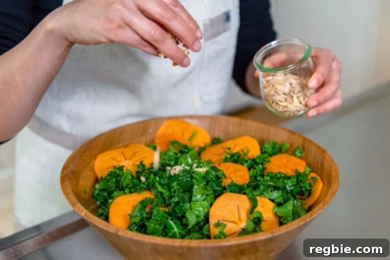 Sprinkling toasted almond slices on top of a kale salad with persimmons.