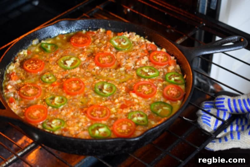 Someone putting a cast iron skillet filled with Nom Nom Paleo's Tex-Mex Beef and Rice Casserole, a grain-free one pan dinner.