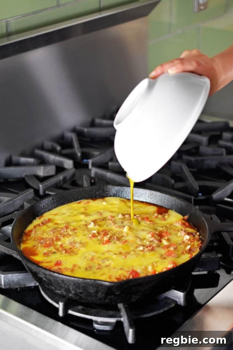 Pouring whisked eggs into a cast iron skillet filled with ingredients to make Whole30 and keto Tex Mex Beef and Rice Casserole.
