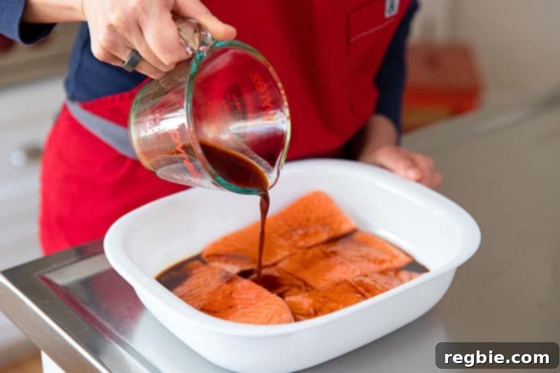 Pouring a measured amount of All-Purpose Stir-Fry Sauce from a glass measuring cup directly onto four raw salmon fillets arranged in a white square container, initiating the marination process.