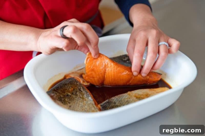 A close-up shot of raw salmon fillets being flipped, ensuring the skin-side is facing up, immersed in the Whole30 compliant teriyaki marinade within a white container.