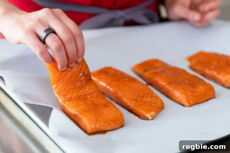 Raw, marinated teriyaki salmon fillets carefully placed skin-side down in the center of a parchment-lined, rimmed baking sheet, ready for the vegetables to be arranged around them.