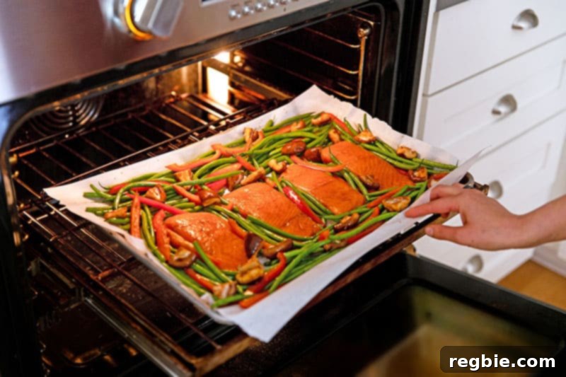 A sheet pan, laden with paleo-friendly teriyaki salmon fillets and roasted vegetables, being carefully slid into a hot oven to cook until perfectly done.