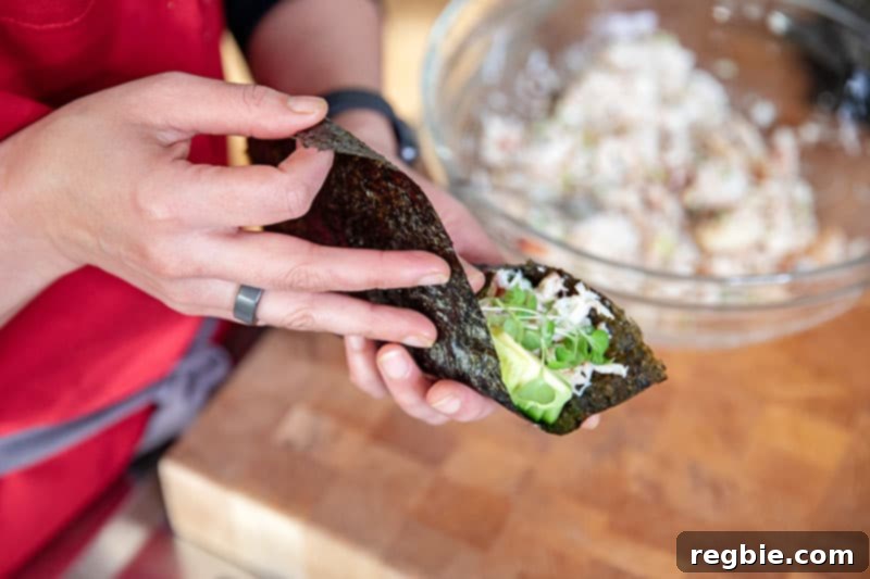 Hands meticulously wrapping a piece of toasted nori around the delicious filling to expertly assemble a homemade California hand roll.
