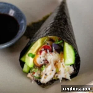 A closeup of a California hand roll on a gray plate next to a small bowl filled with coconut aminos.