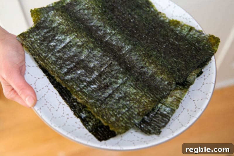 A person expertly holding a white plate laden with toasted nori sheets, carefully cut in half, ready to be filled and transformed into delectable California hand rolls or Temaki.