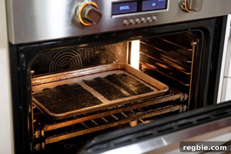 Two sheets of nori, arranged in a single layer on a rimmed baking sheet, are being gently toasted under an oven broiler to prepare them for delicious sushi.