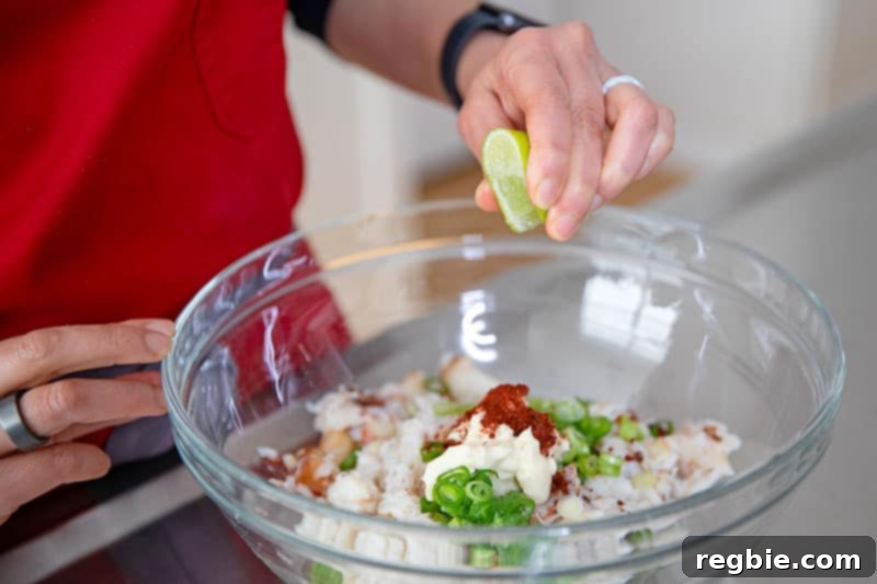 A hand squeezing fresh lime juice into a bowl containing the vibrant filling ingredients for Whole30 and keto California sushi hand rolls, enhancing the flavors.