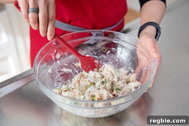 A red silicone spatula is used to gently mix the flavorful filling for gluten-free and low carb California sushi hand rolls in a mixing bowl.