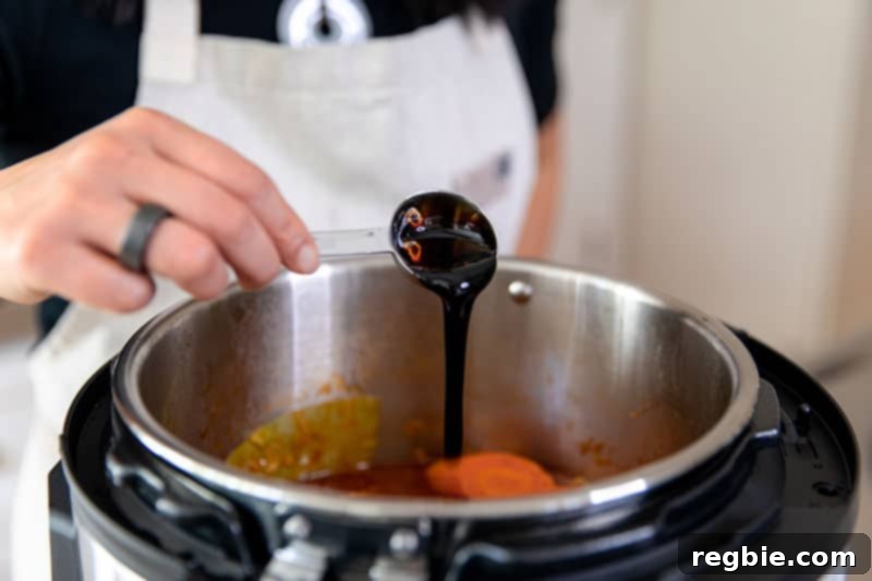 Easy Instant Pot Whole30 Keto Pork Stew 14 Pouring a spoonful of aged balsamic vinegar into the Instant Pot, adding a final touch of flavor to the Whole30 pork and cabbage stew.