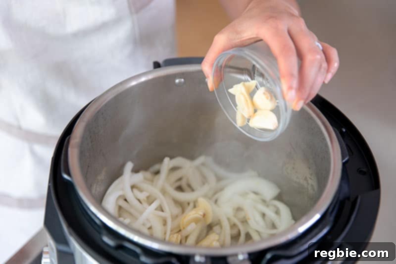 Easy Instant Pot Whole30 Keto Pork Stew 6 Adding smashed and peeled garlic cloves to the sautéed onions in an open Instant Pot, enhancing the flavor of the paleo pork and cabbage stew.