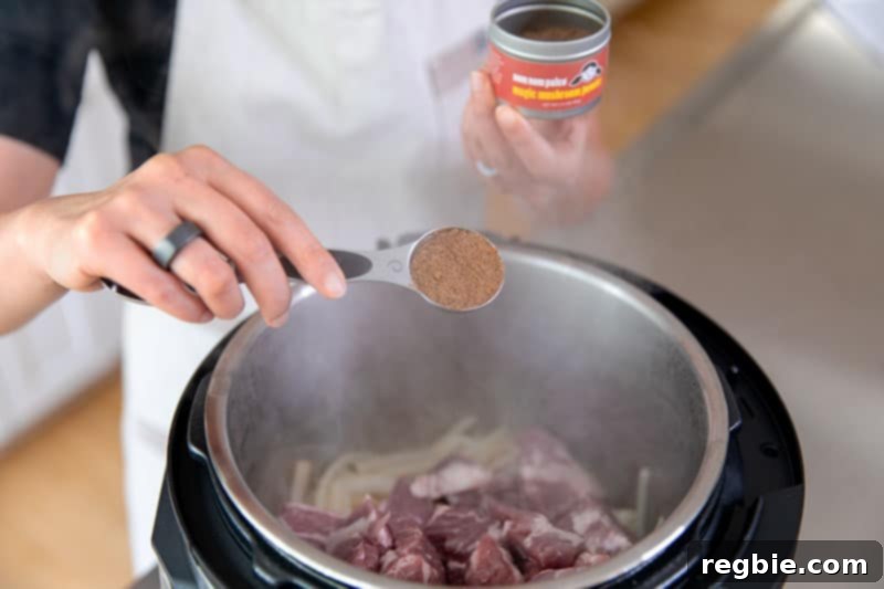 Easy Instant Pot Whole30 Keto Pork Stew 7 Adding a spoonful of Magic Mushroom Powder to the Instant Pot, alongside pork, onions, and garlic, for a flavor boost.