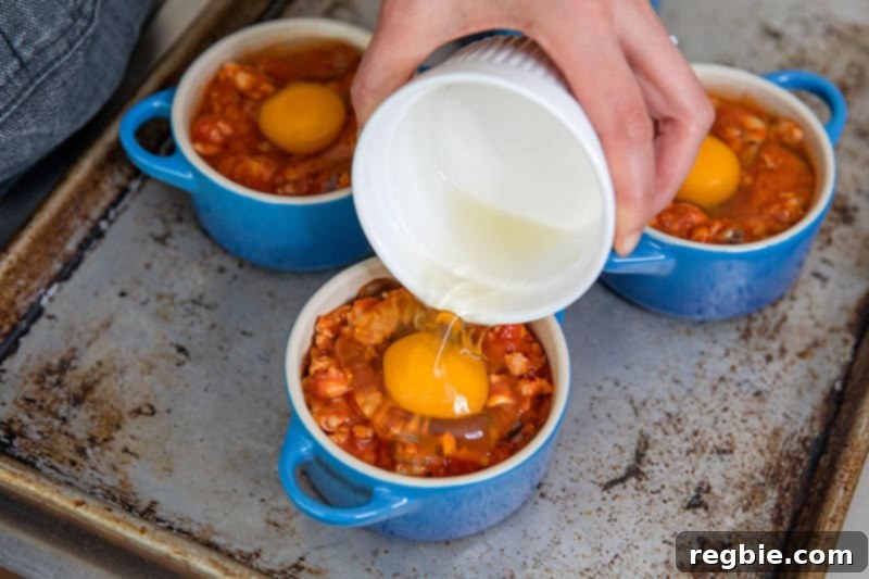 Inferno Eggs 12 Someone pouring in a raw egg into a blue cocotte filled with spicy tomato meat sauce