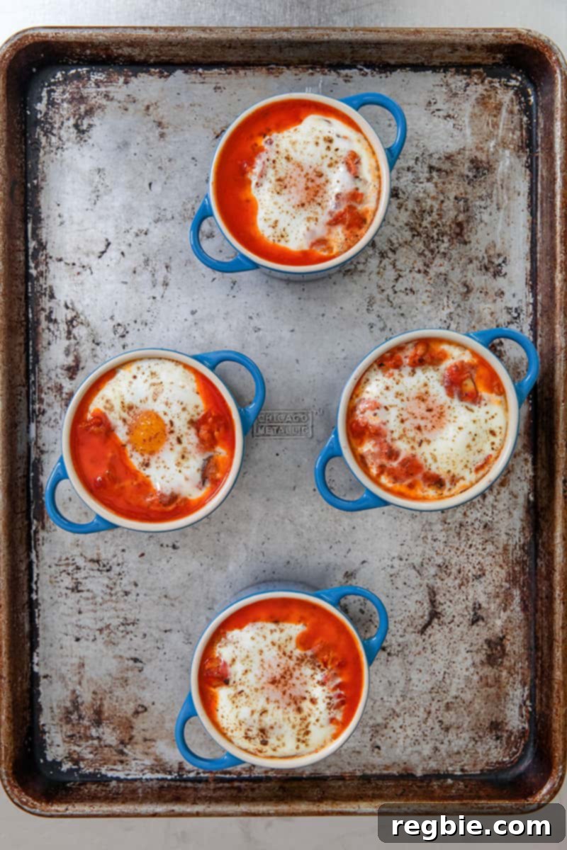 Inferno Eggs 15 An overhead shot of a rimmed baking sheet topped with four blue cocottes filled with paleo eggs in purgatory right out of the oven.
